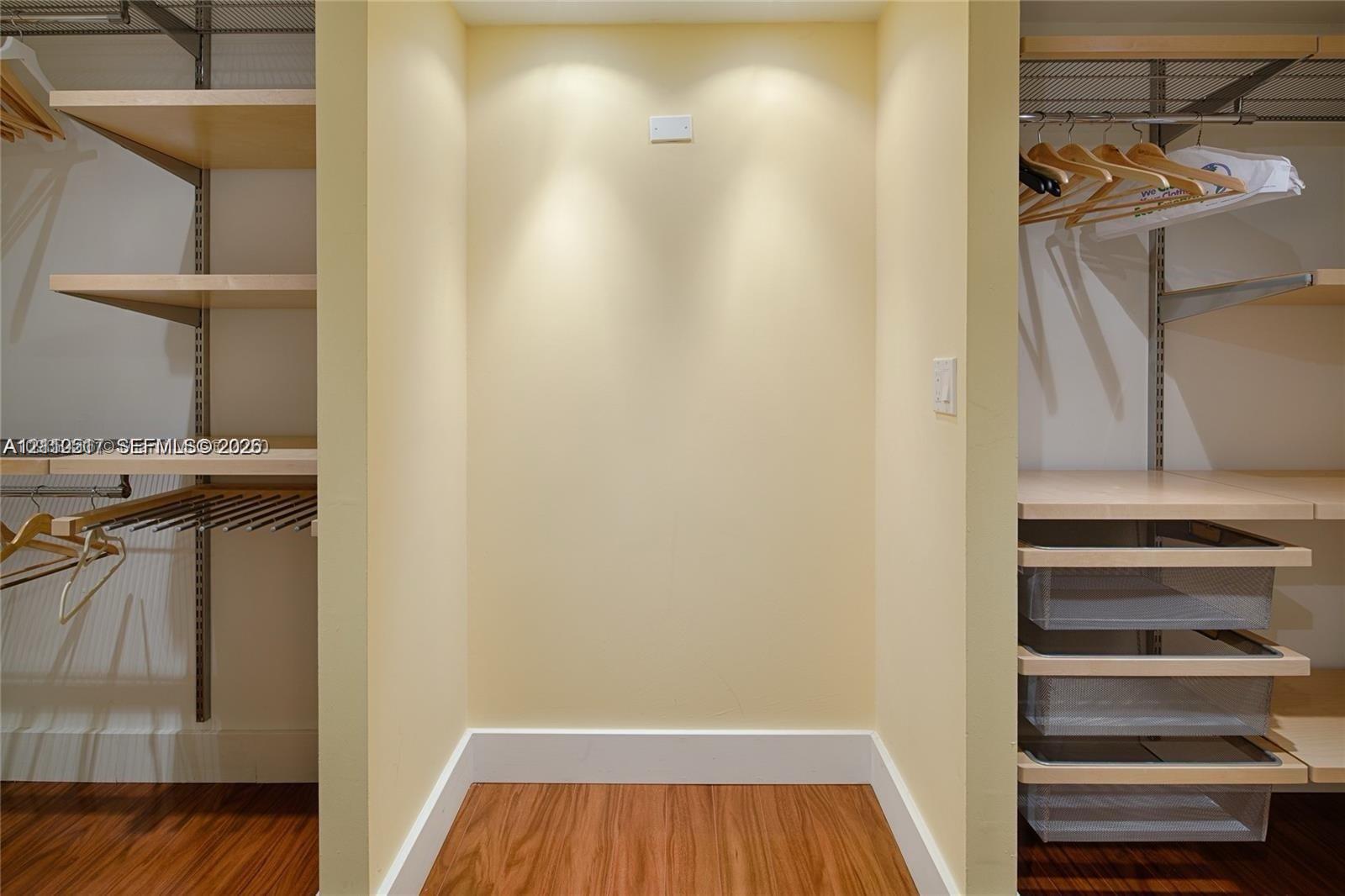 Walk-in closet featuring adjustable light wood-finish shelving, integrated hanging rods, and built-in translucent sliding storage drawers with wood-finish flooring Walk-in closet featuring adjustable light wood-finish shelving, integrated hanging rods, and built-in translucent sliding storage drawers with wood-finish flooring