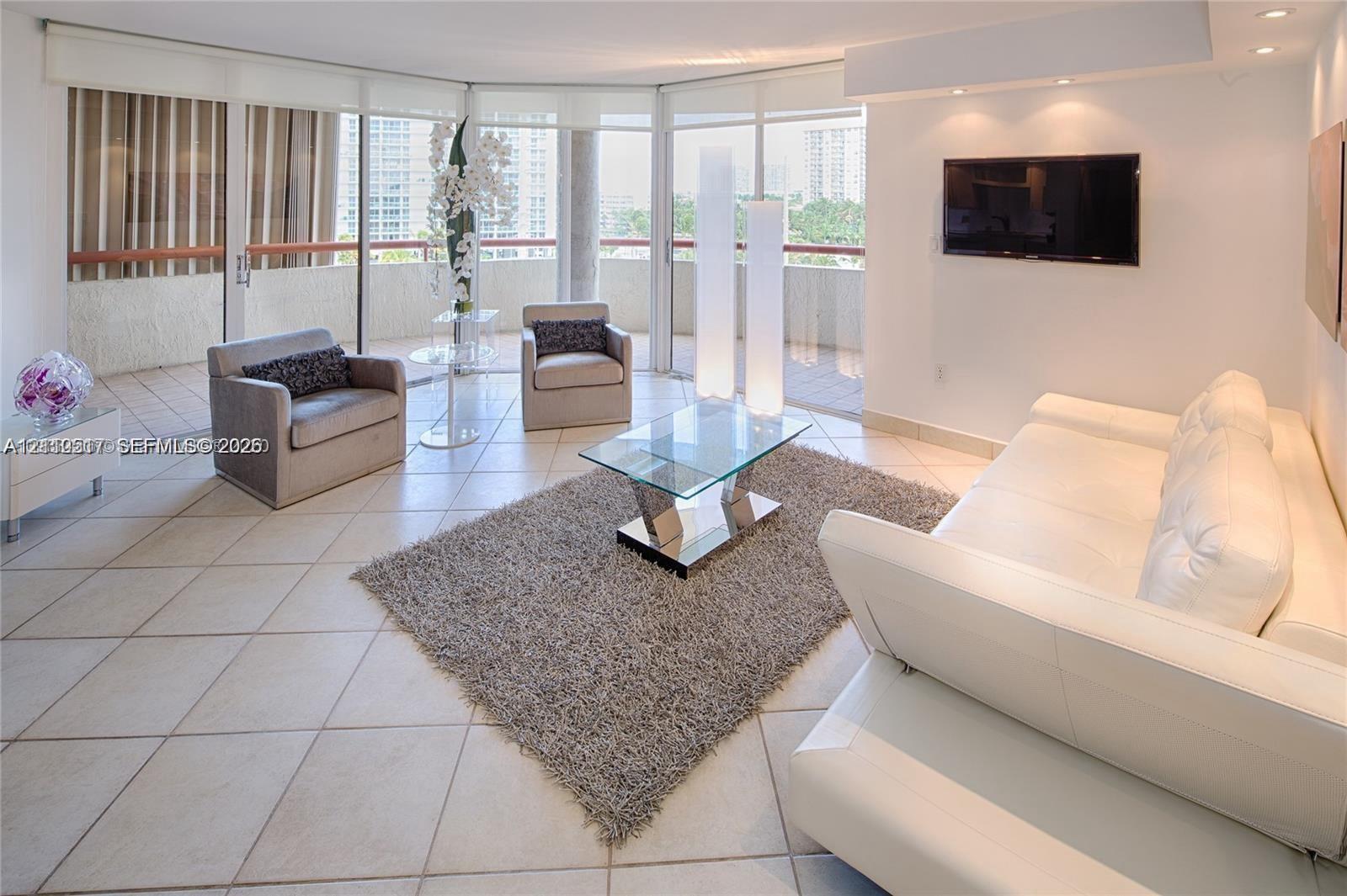 Expansive living area featuring light-toned tile flooring, recessed ceiling lighting, and floor-to-ceiling glass sliding doors providing access to a private balcony Expansive living area featuring light-toned tile flooring, recessed ceiling lighting, and floor-to-ceiling glass sliding doors providing access to a private balcony