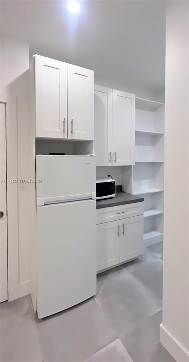 White cabinetry with brushed metal hardware, dark solid-surface countertop, and built-in open shelving