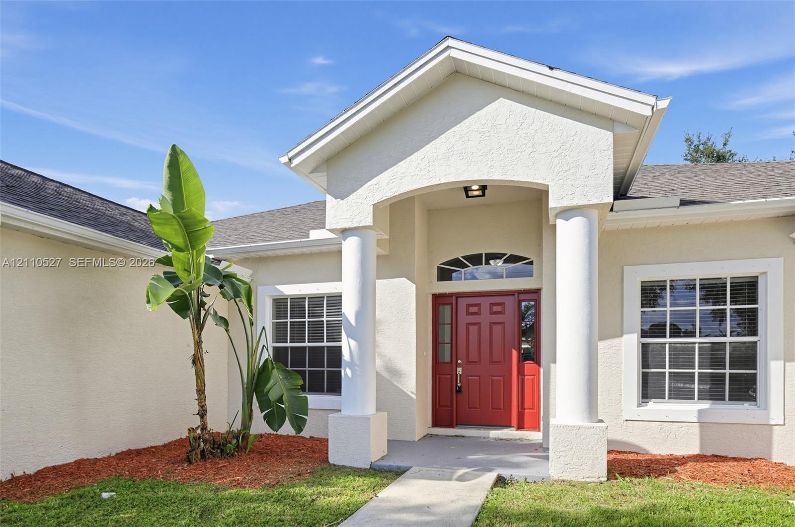 Stucco exterior featuring an arched entryway with decorative columns, a prominent red entry door with sidelights, and a transom window
