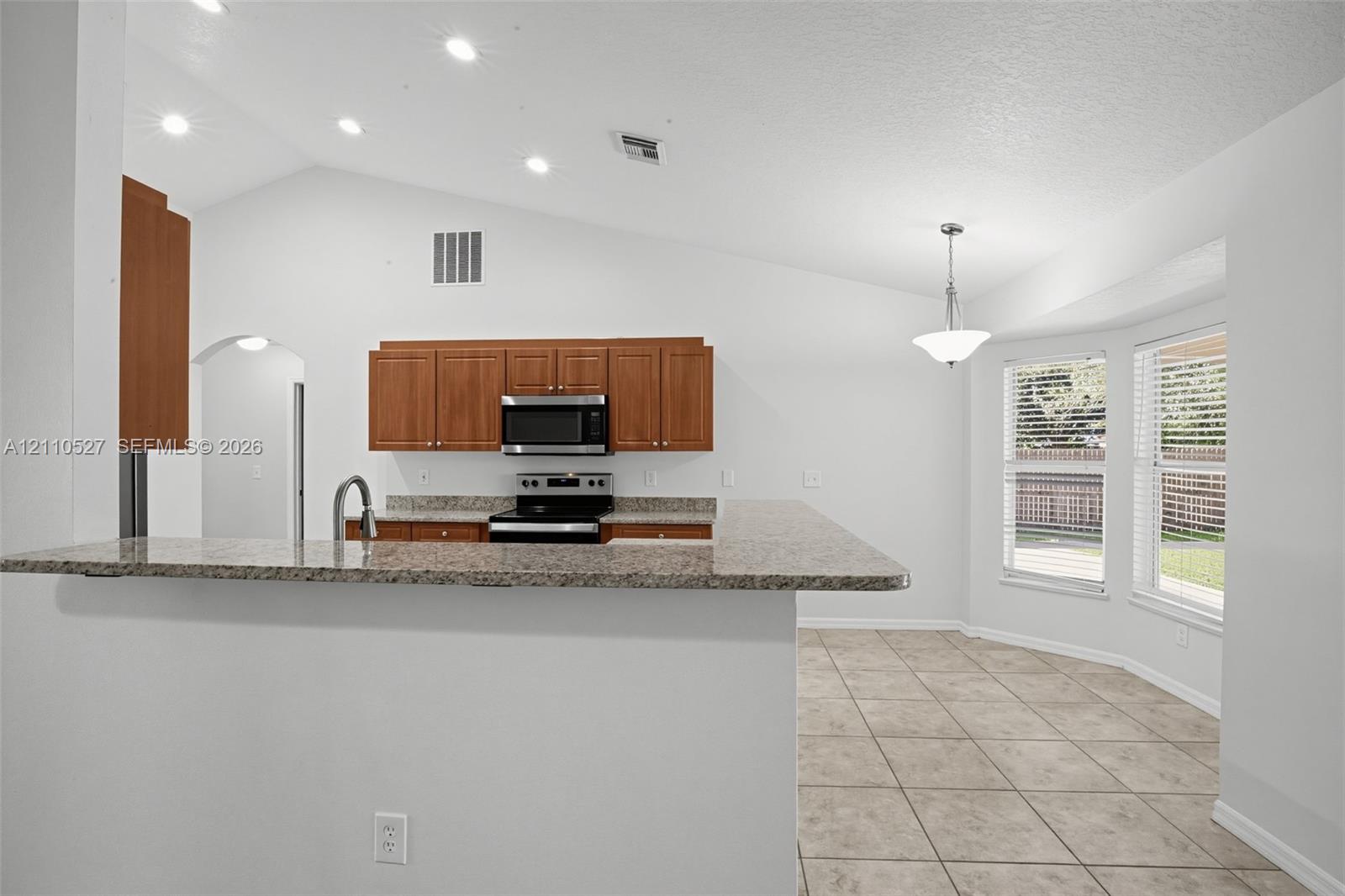 Kitchen featuring a stone-look countertop, wood cabinetry, recessed lighting, tile flooring, and vaulted ceilings