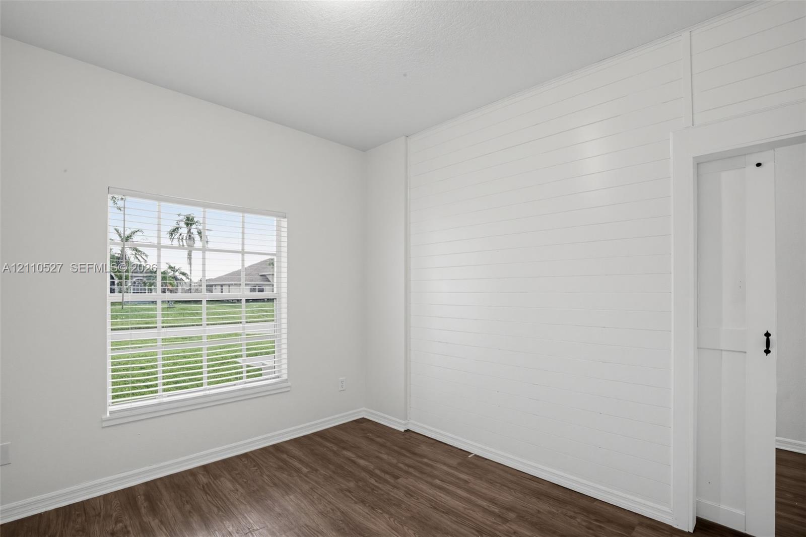 Interior space featuring wood-finish flooring, horizontal shiplap wall accent, multi-pane window with white blinds, and a white sliding door with black hardware