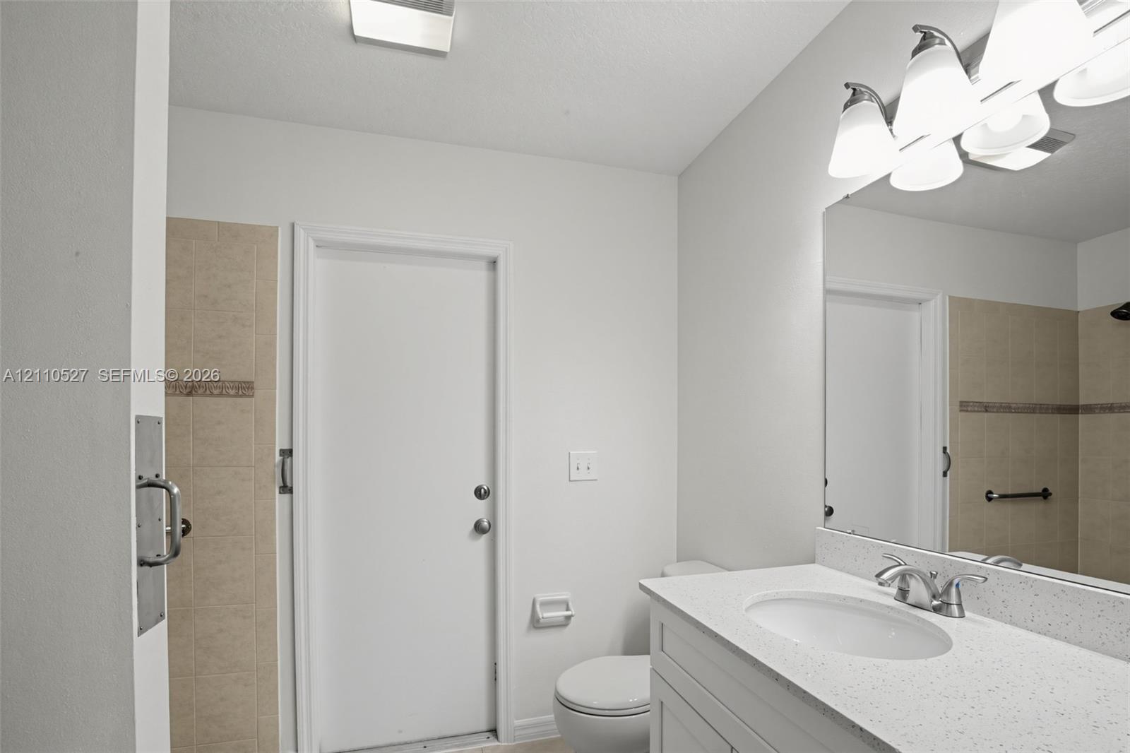 Bathroom featuring a white vanity with a quartz countertop, an integrated sink, a large wall-mounted mirror, and tile-surround shower area