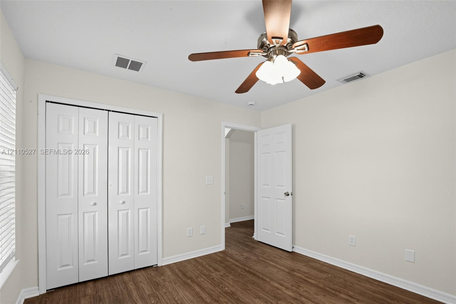 Room featuring wood-finish flooring, a ceiling fan with integrated three-bulb light fixture, and a white six-panel closet door