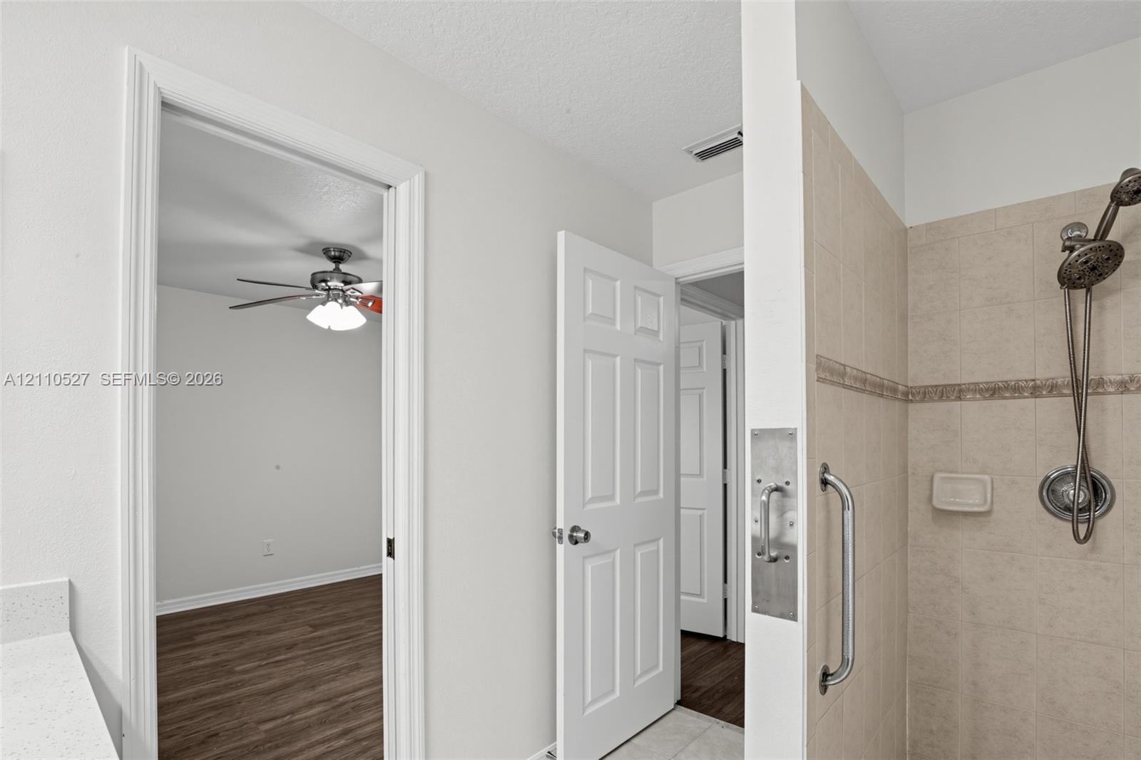 Shower stall with ceramic tile surround, handheld shower fixture, and metal grab bar, featuring a quartz-topped vanity