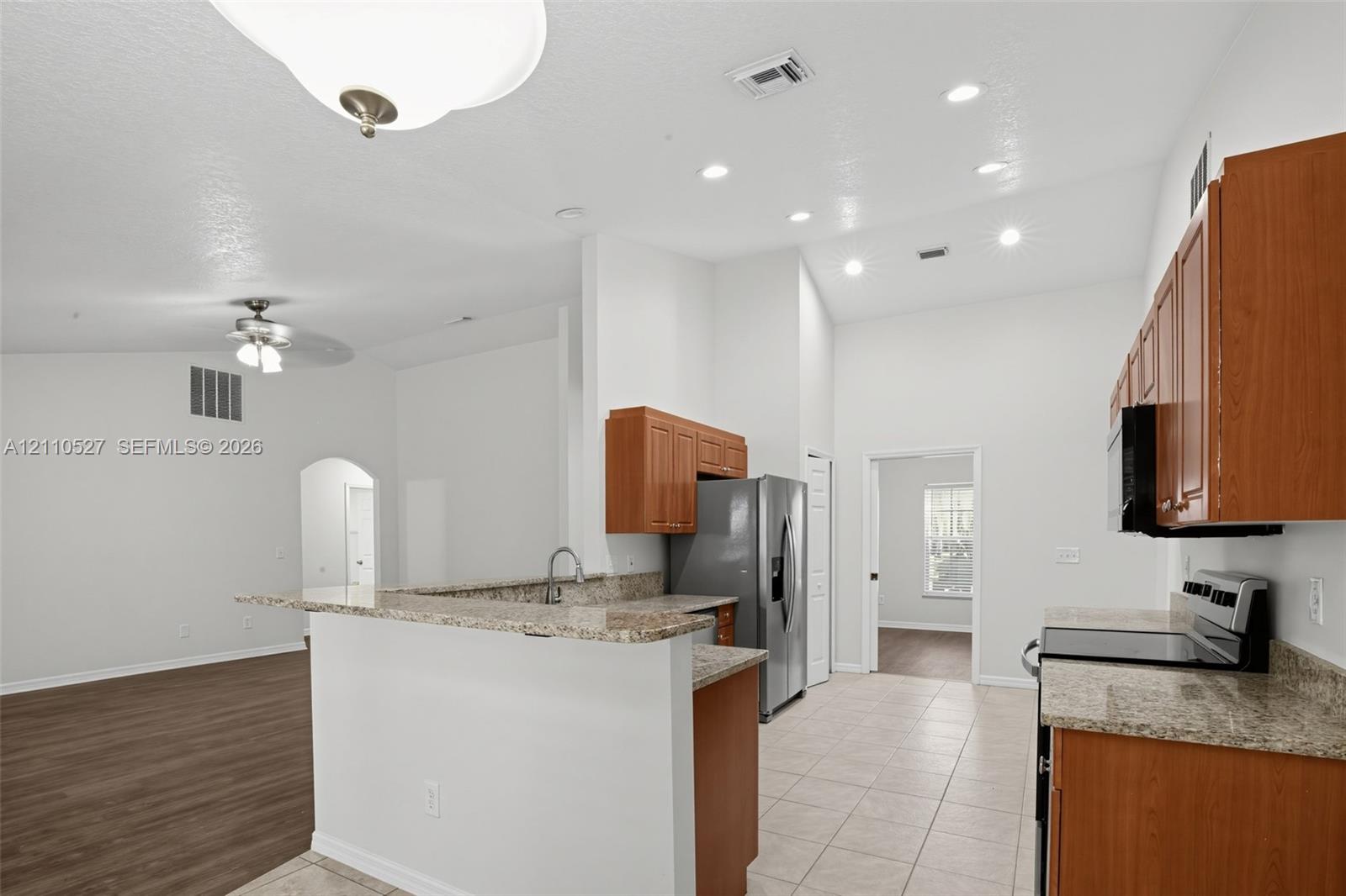 Kitchen featuring wood cabinetry, stone-finish countertops, stainless steel appliances, recessed ceiling lighting, and tiled flooring