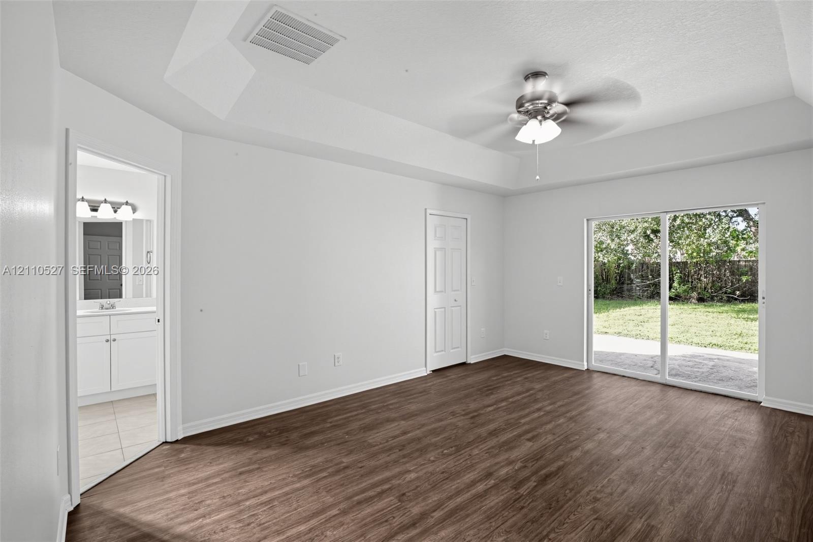 Room featuring wood-finish flooring, tray ceiling with a central ceiling fan, and sliding glass doors with exterior patio access