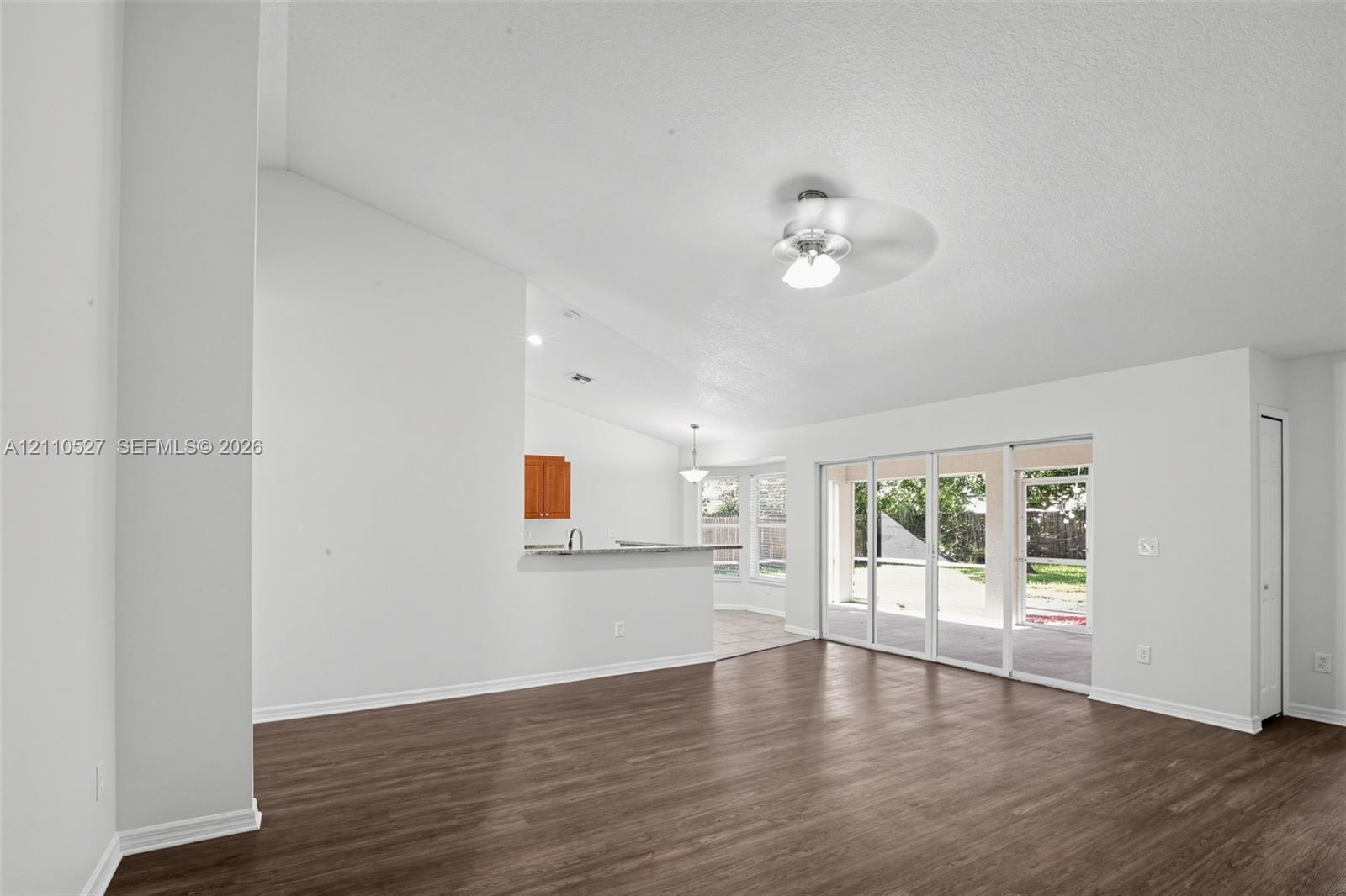 Open living area featuring vaulted ceilings, wood-finish flooring, a ceiling fan, and sliding glass doors with exterior access