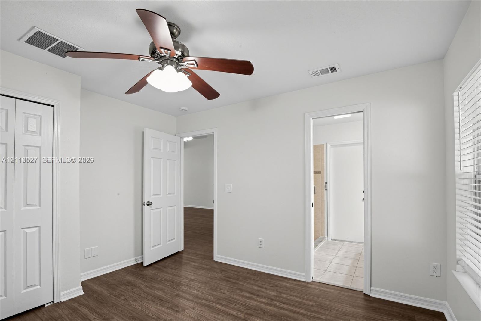 Room featuring wood-finish flooring, a multi-blade ceiling fan with integrated lighting, a six-panel closet door, and a white window with horizontal blinds