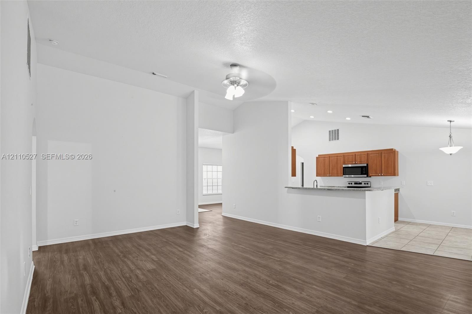 Vaulted ceilings, wood-finish flooring, kitchen featuring stone-surface countertops, wood cabinetry, and stainless steel built-in microwave