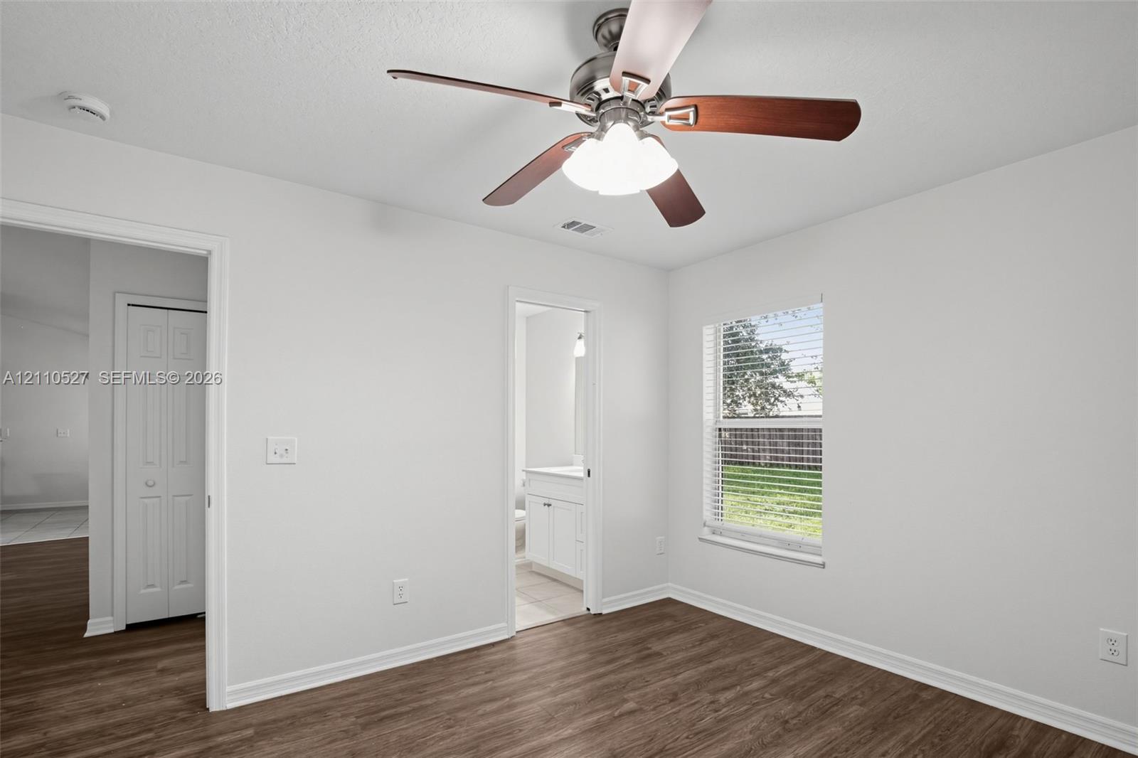 Room featuring wood-finish flooring, a multi-blade ceiling fan with integrated lighting, and a window with horizontal blinds