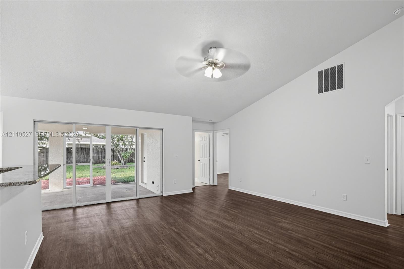 Open-concept living space featuring vaulted ceilings, wood-finish flooring, a ceiling fan with light fixture, and sliding glass doors