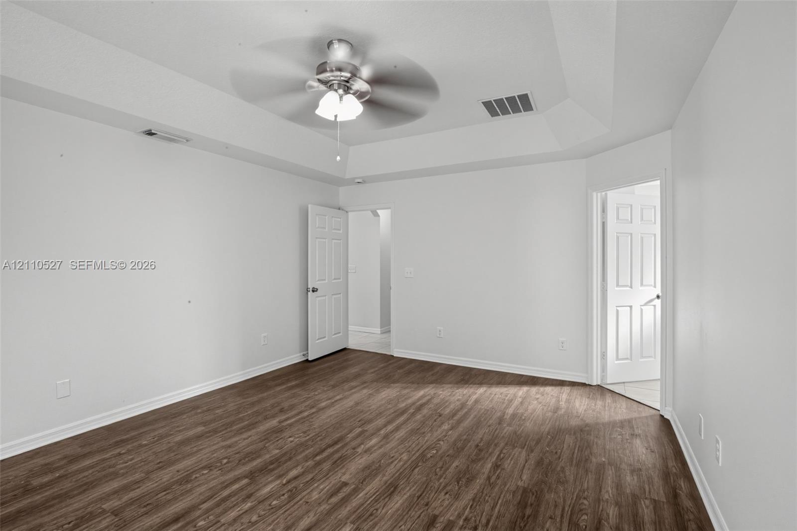 Tray ceiling featuring a central brushed-nickel ceiling fan with integrated lighting and wood-finish flooring