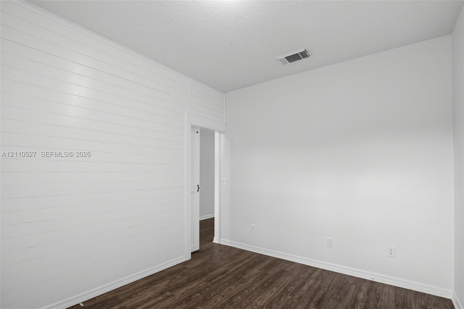 Room featuring horizontal shiplap wall paneling, dark wood-finish flooring, and a door opening