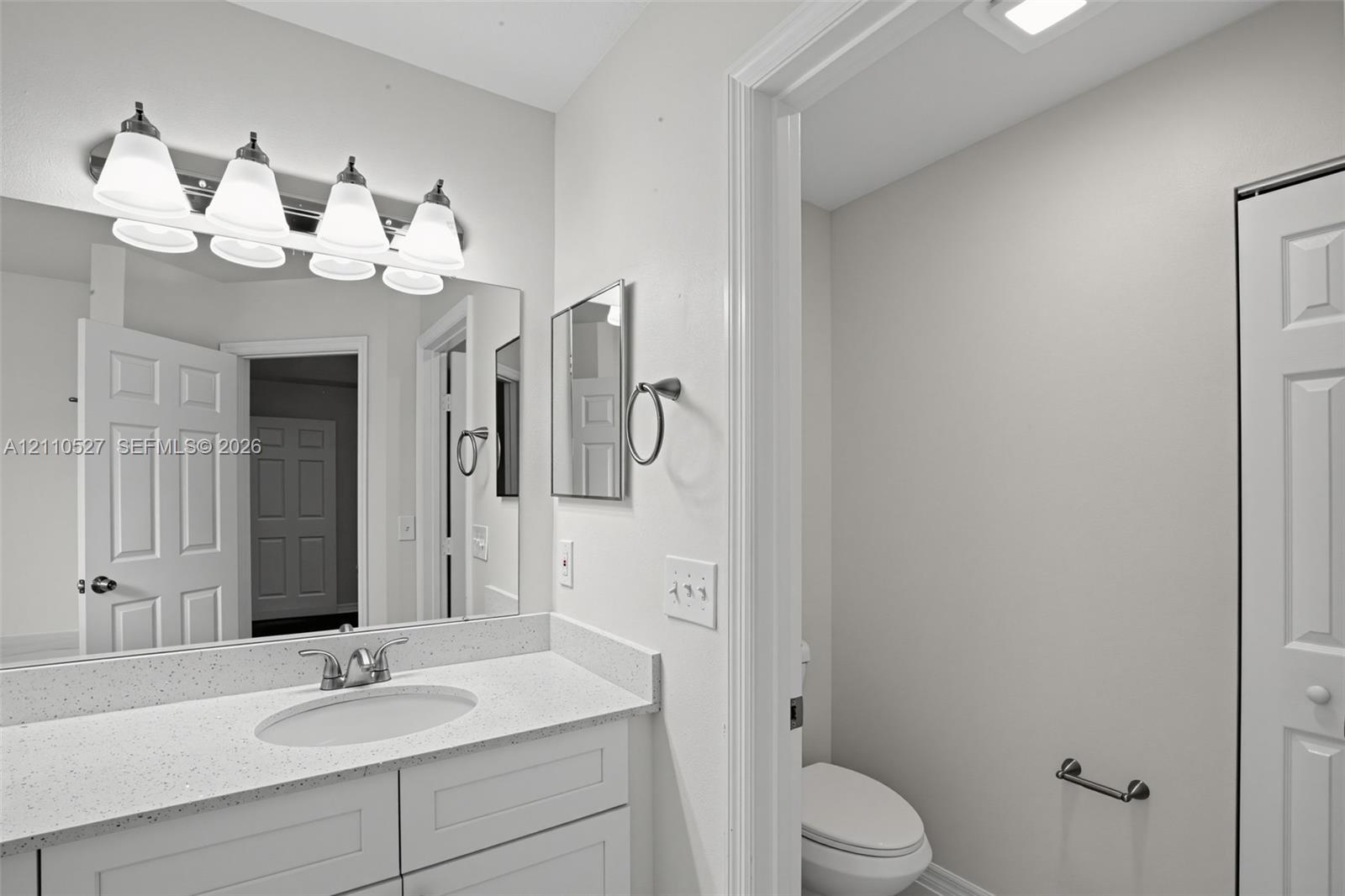 Bathroom vanity featuring an integrated oval sink, stone-composite countertop, shaker-style cabinetry, a wall-to-wall mirror, and a four-light fixture