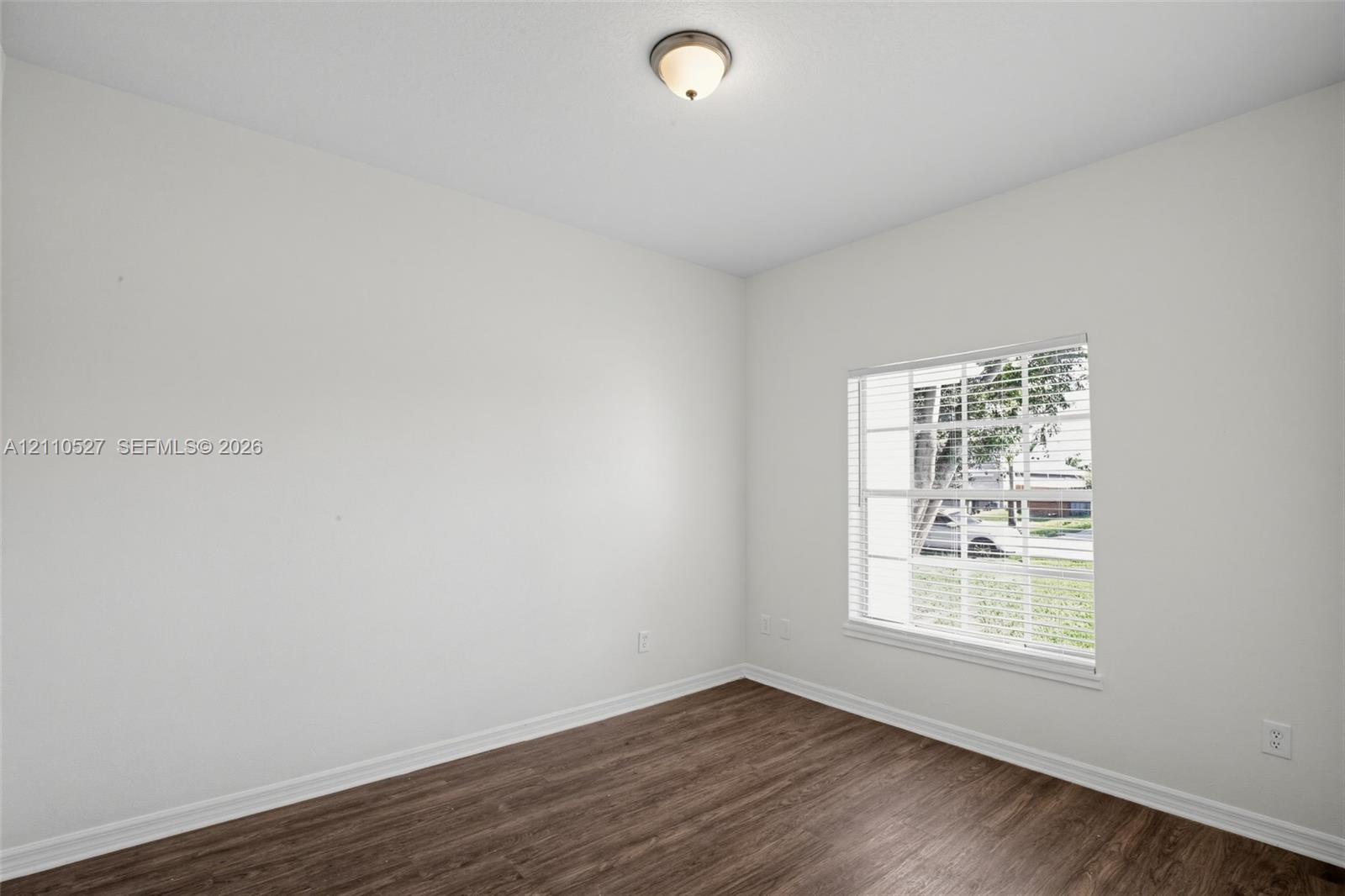 Room featuring neutral-toned walls, wood-finish flooring, a multi-pane window with integrated blinds, and a dome-style flush-mount ceiling light