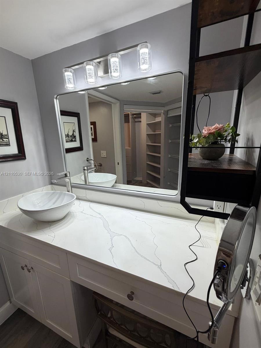 White vanity with a stone-finish countertop, round vessel sink, chrome faucet, rectangular mirror, and a four-light fixture