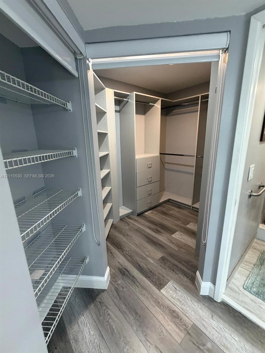Walk-in closet featuring wood-finish flooring, built-in shelving, integrated dresser drawers, and metal wire rack storage