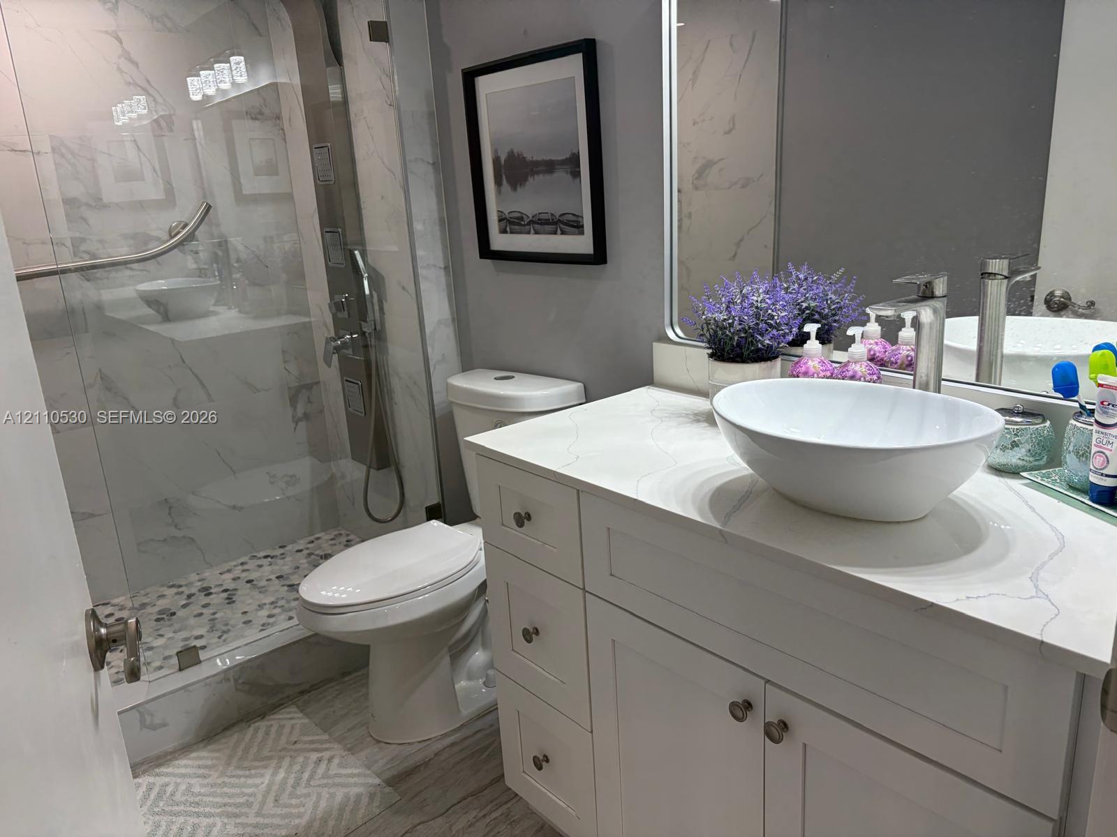 Bathroom featuring a vanity with a white vessel sink, quartz countertop, walk-in shower with stone-tile flooring, floor-to-ceiling tile surround, and polished hardware