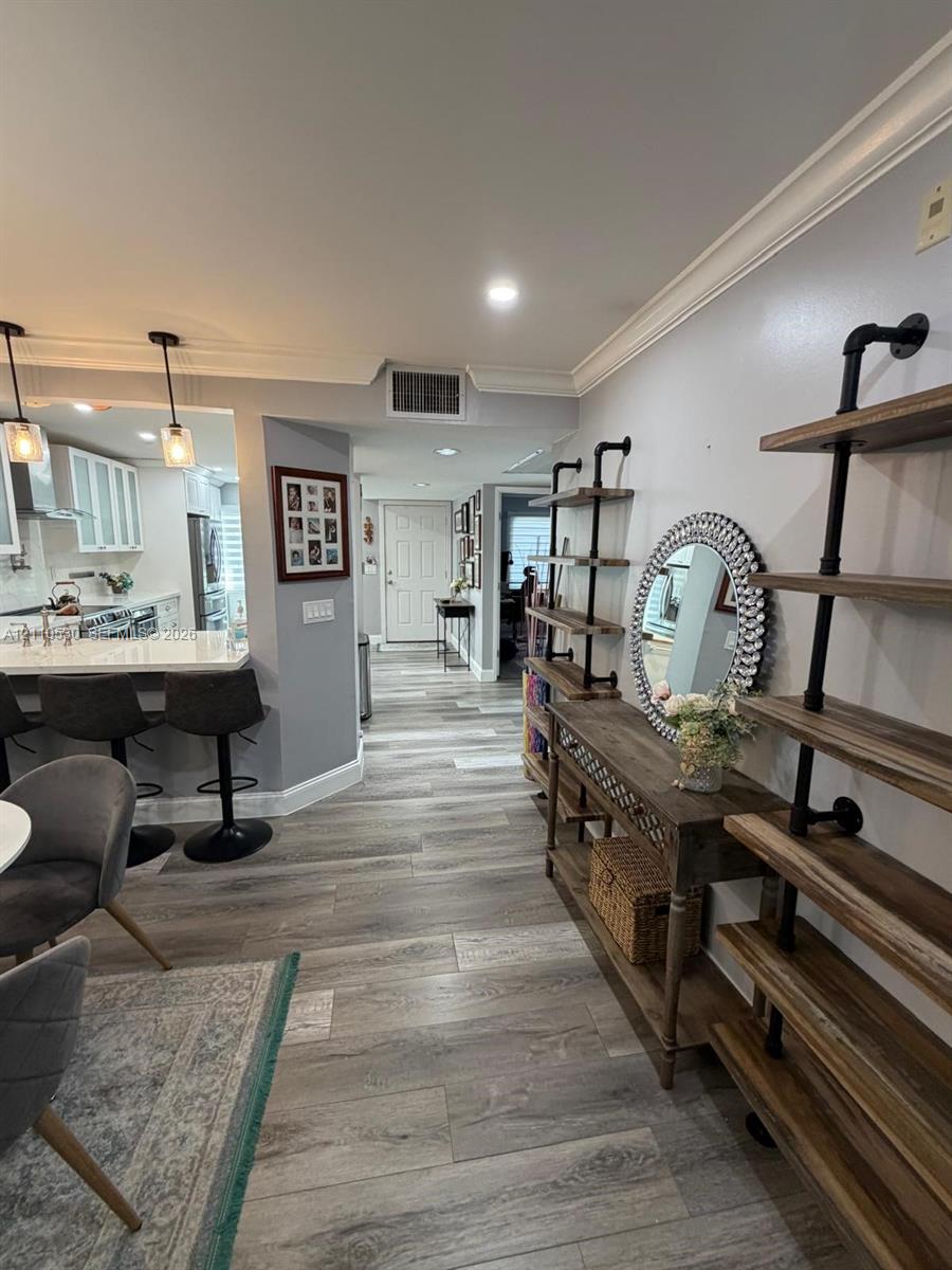 Wood-finish flooring, crown molding, recessed lighting, and kitchen peninsula featuring quartz countertops and pendant lighting