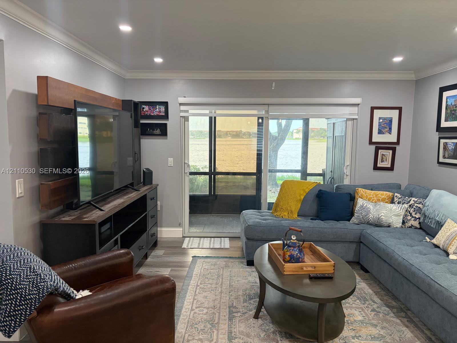 Living area featuring wood-finish flooring, recessed lighting, crown molding, and large sliding glass doors opening to a screened enclosure