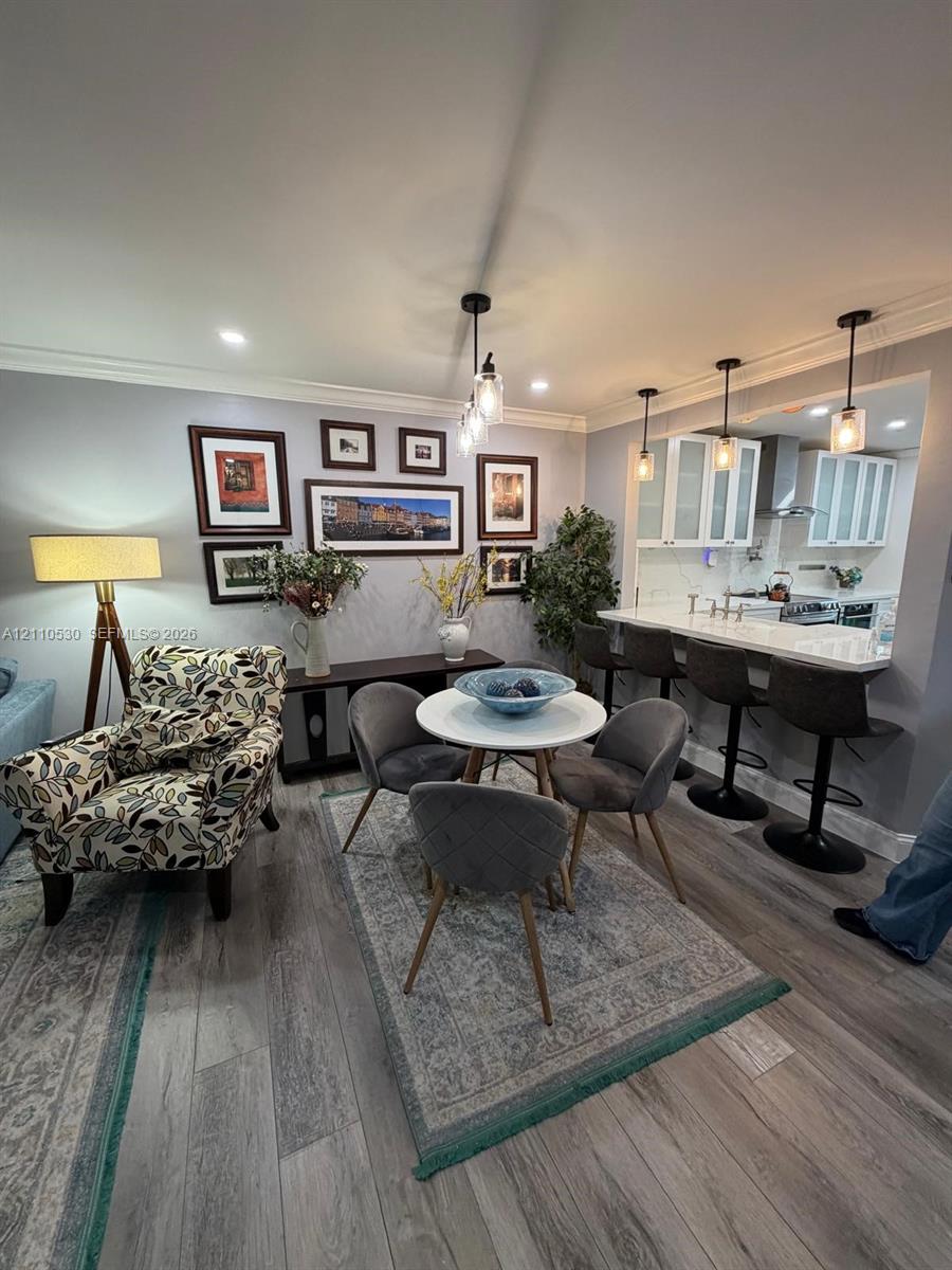 Open-concept kitchen area featuring a stone-topped breakfast bar, recessed ceiling lighting, glass-paneled cabinetry, wood-finish flooring, and crown molding Open-concept kitchen area featuring a stone-topped breakfast bar, recessed ceiling lighting, glass-paneled cabinetry, wood-finish flooring, and crown molding