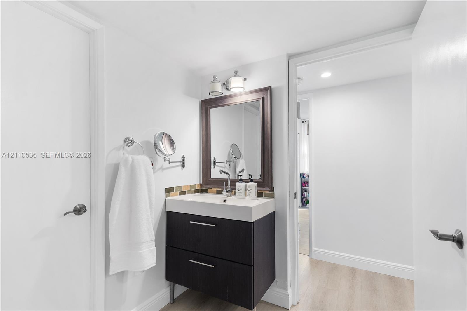 Dark wood-finish vanity with two drawers, integrated white basin, framed wall mirror, multi-toned tile backsplash, and dual-light fixture Dark wood-finish vanity with two drawers, integrated white basin, framed wall mirror, multi-toned tile backsplash, and dual-light fixture
