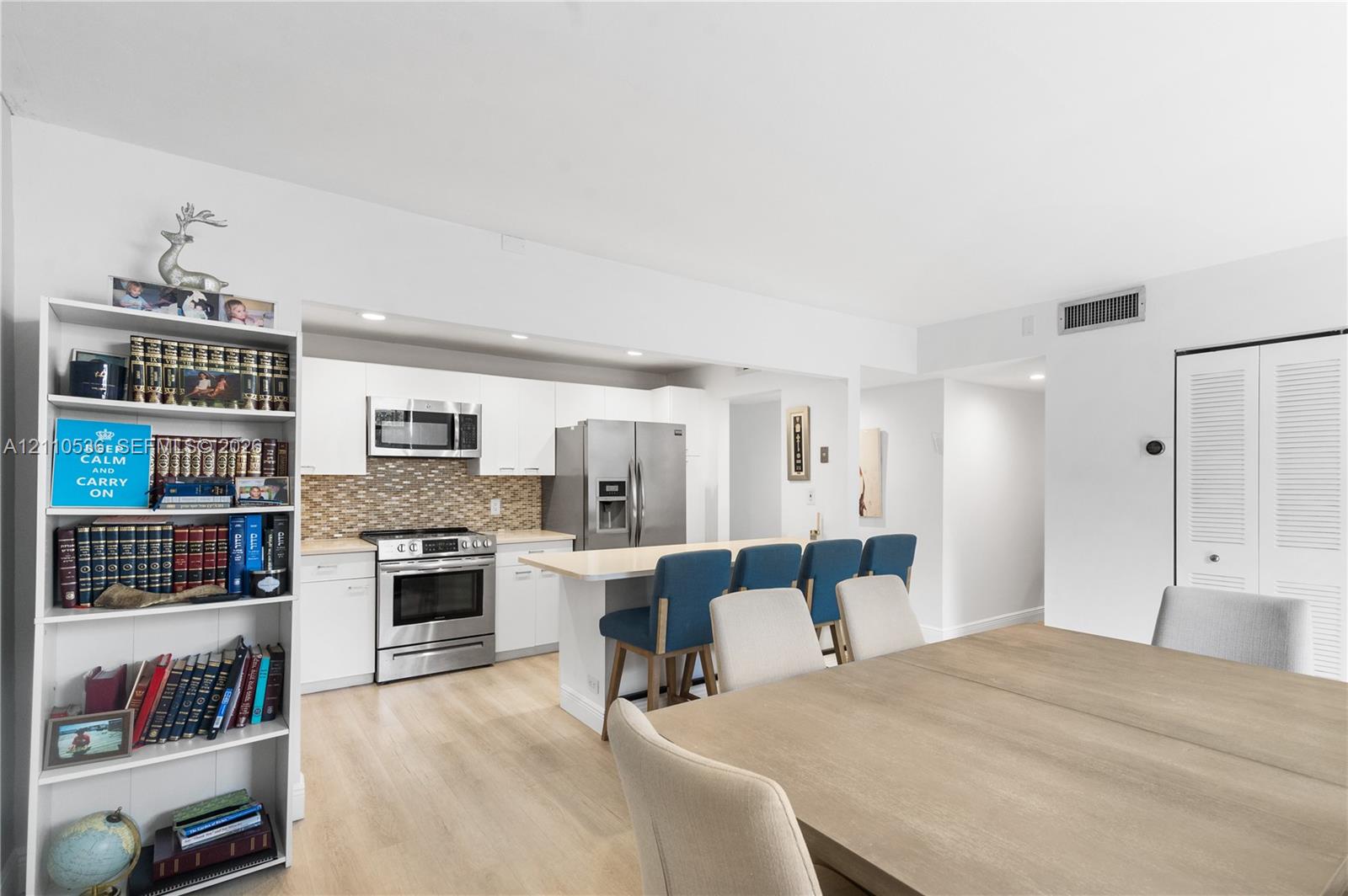 Kitchen featuring white cabinetry, stainless steel appliances, a center island with counter seating, and a decorative tile backsplash, complemented by wood-finish flooring Kitchen featuring white cabinetry, stainless steel appliances, a center island with counter seating, and a decorative tile backsplash, complemented by wood-finish flooring
