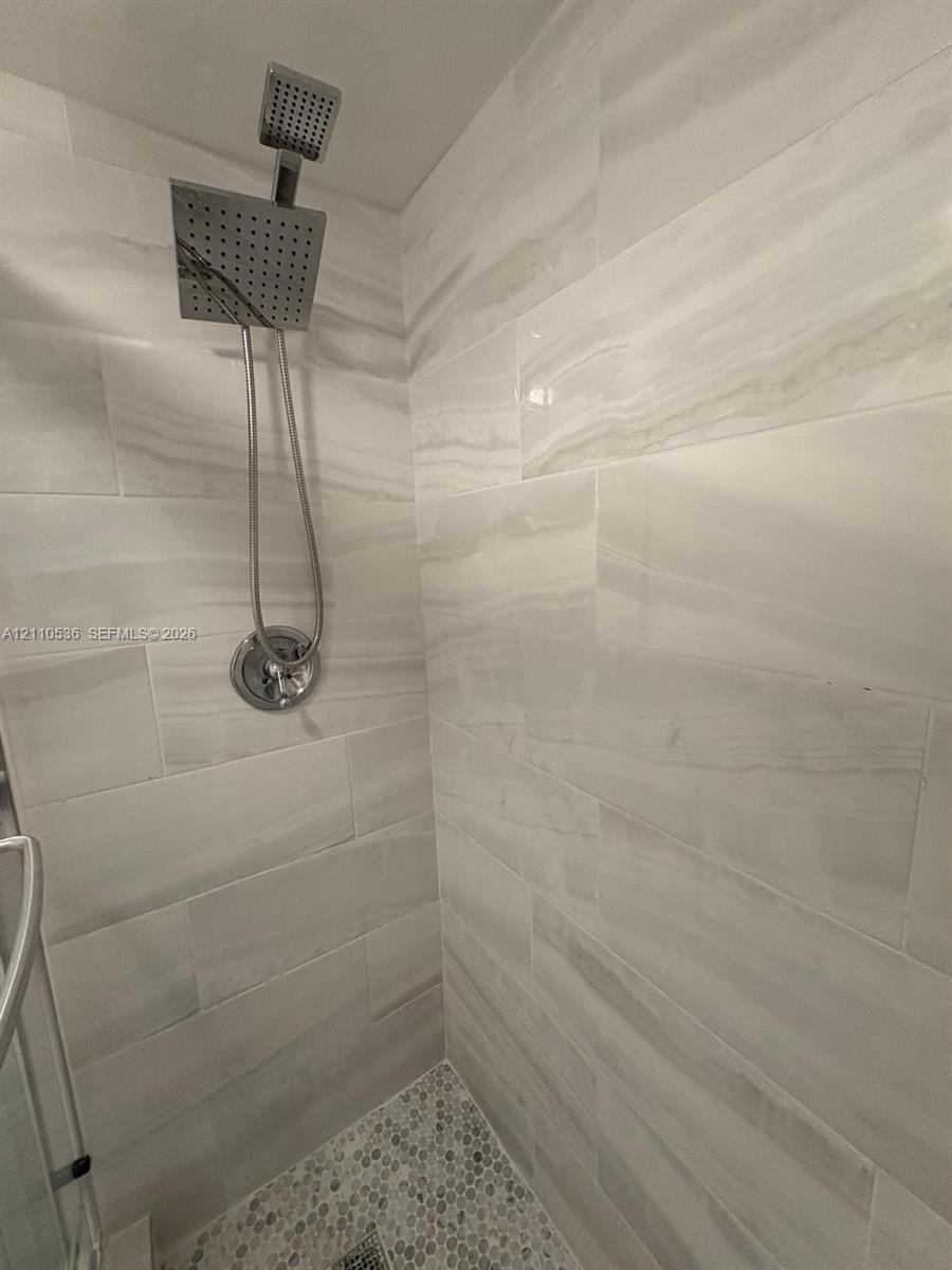 Shower stall featuring large-format stone-patterned wall tile, pebble-texture floor tile, and a polished chrome square rainfall showerhead with a handheld sprayer Shower stall featuring large-format stone-patterned wall tile, pebble-texture floor tile, and a polished chrome square rainfall showerhead with a handheld sprayer