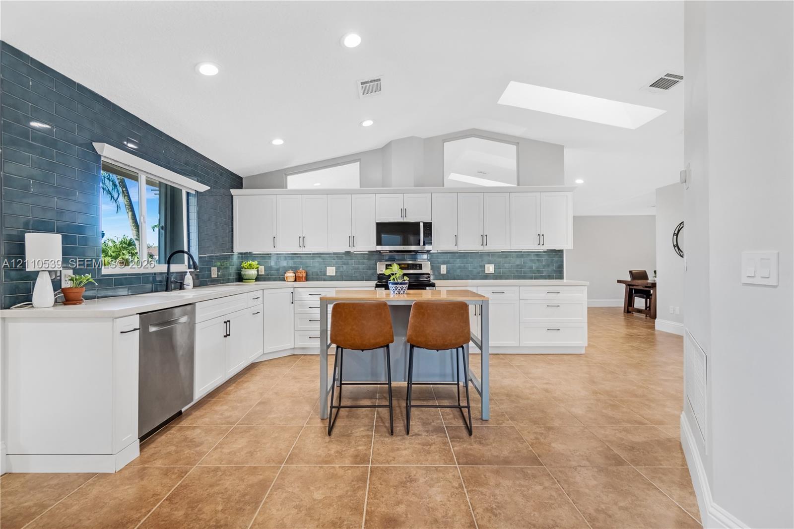 Kitchen featuring white cabinetry, blue tiled backsplash, stainless steel appliances, kitchen island, and vaulted ceilings with integrated skylights