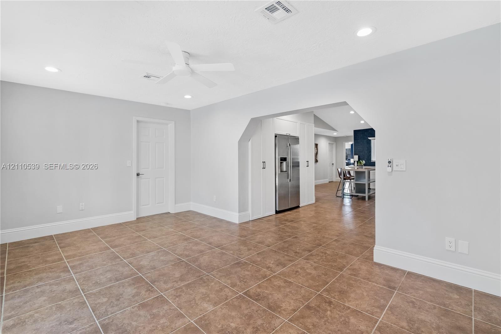 Neutral-toned interior featuring ceramic tile flooring, recessed lighting, a white ceiling fan, and a stainless steel side-by-side refrigerator built into custom cabinetry