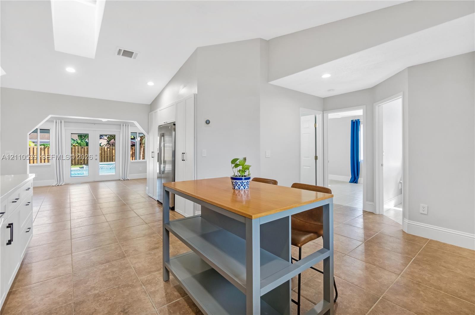 Vaulted ceiling with recessed lighting, neutral tile flooring, white cabinetry, and glass paneled double doors