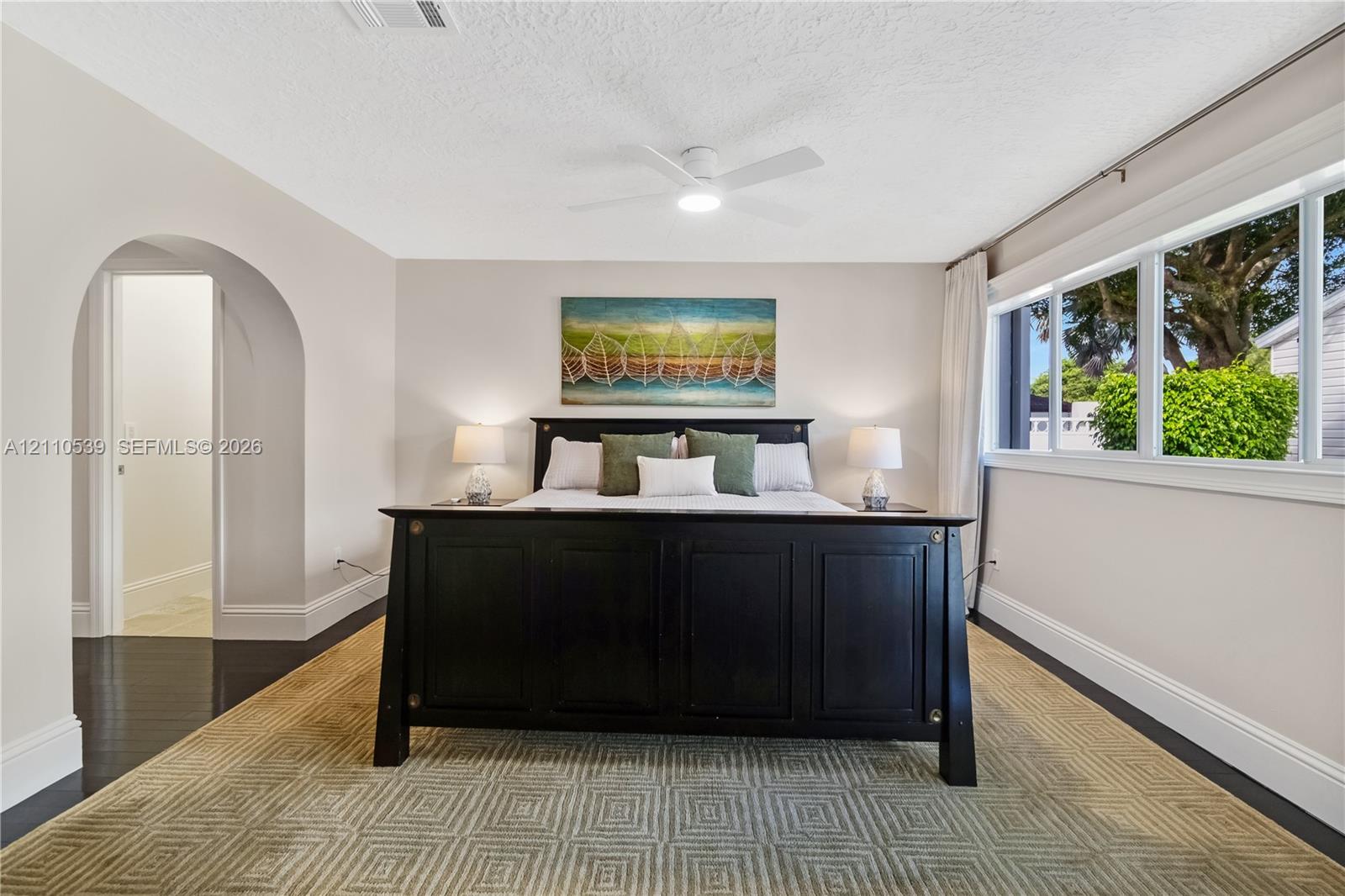 Neutral-toned walls with an arched entryway, wood-finish flooring, a ceiling-mounted light fixture with fan, and expansive horizontal windows