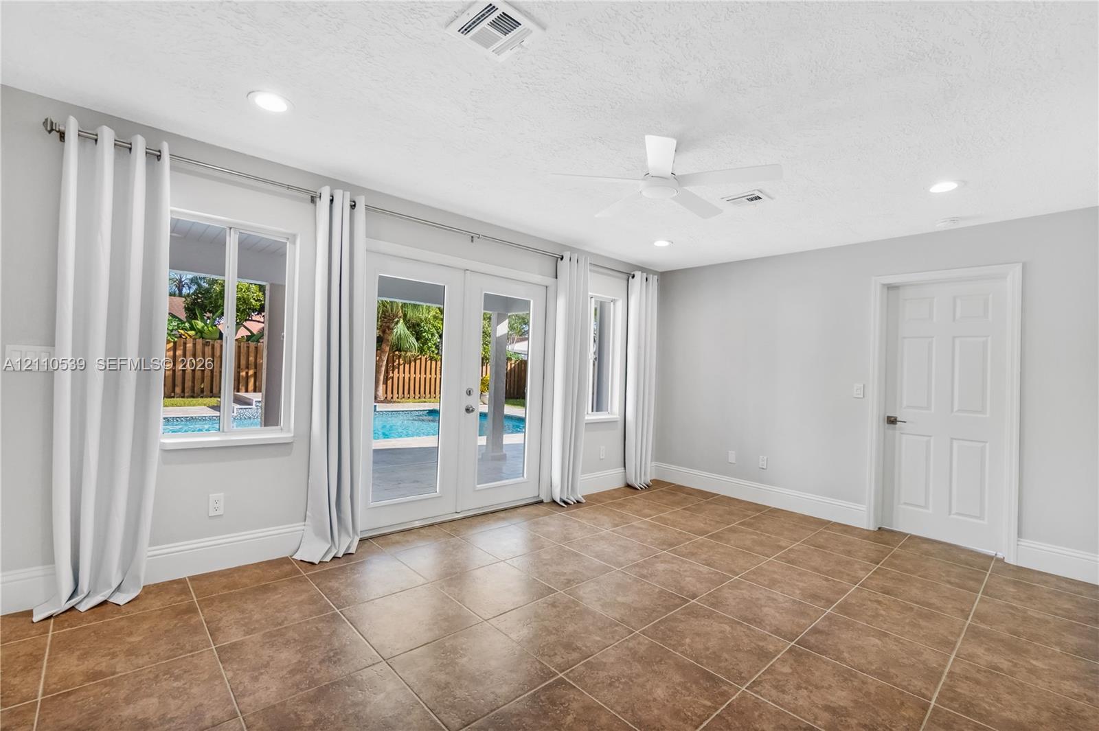 Large-format tile flooring, recessed ceiling lighting, ceiling fan, and double glass doors providing external access