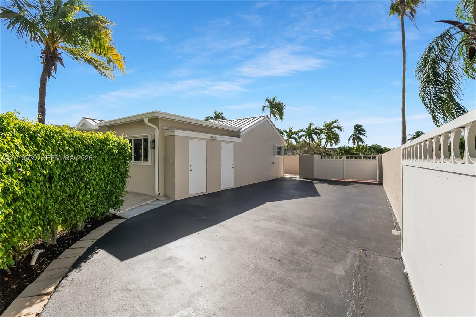 Asphalt driveway leading to a residence featuring smooth exterior wall finishes, double exterior access doors, and decorative perimeter fencing