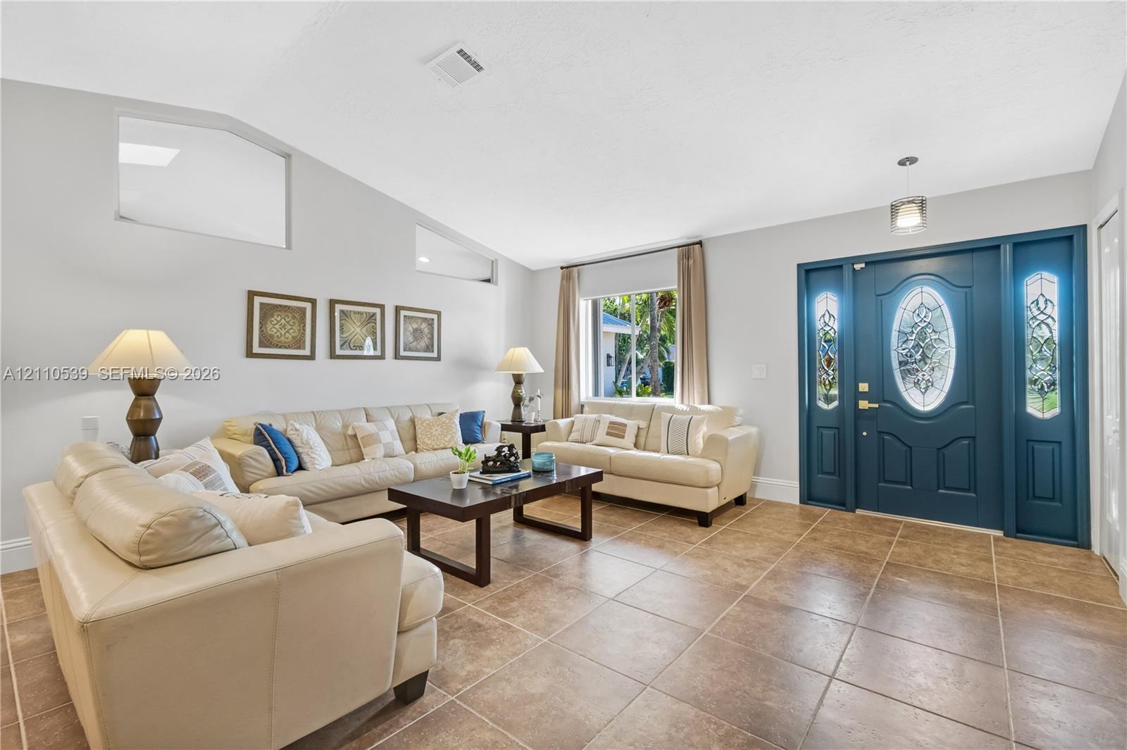 Vaulted ceilings, large-format tile flooring, transom windows, and a decorative front door featuring dual glass-paneled sidelights