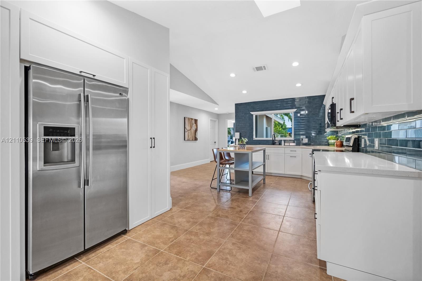 Kitchen featuring white shaker-style cabinetry, stainless steel refrigerator, tile flooring, recessed lighting, and a blue tile backsplash