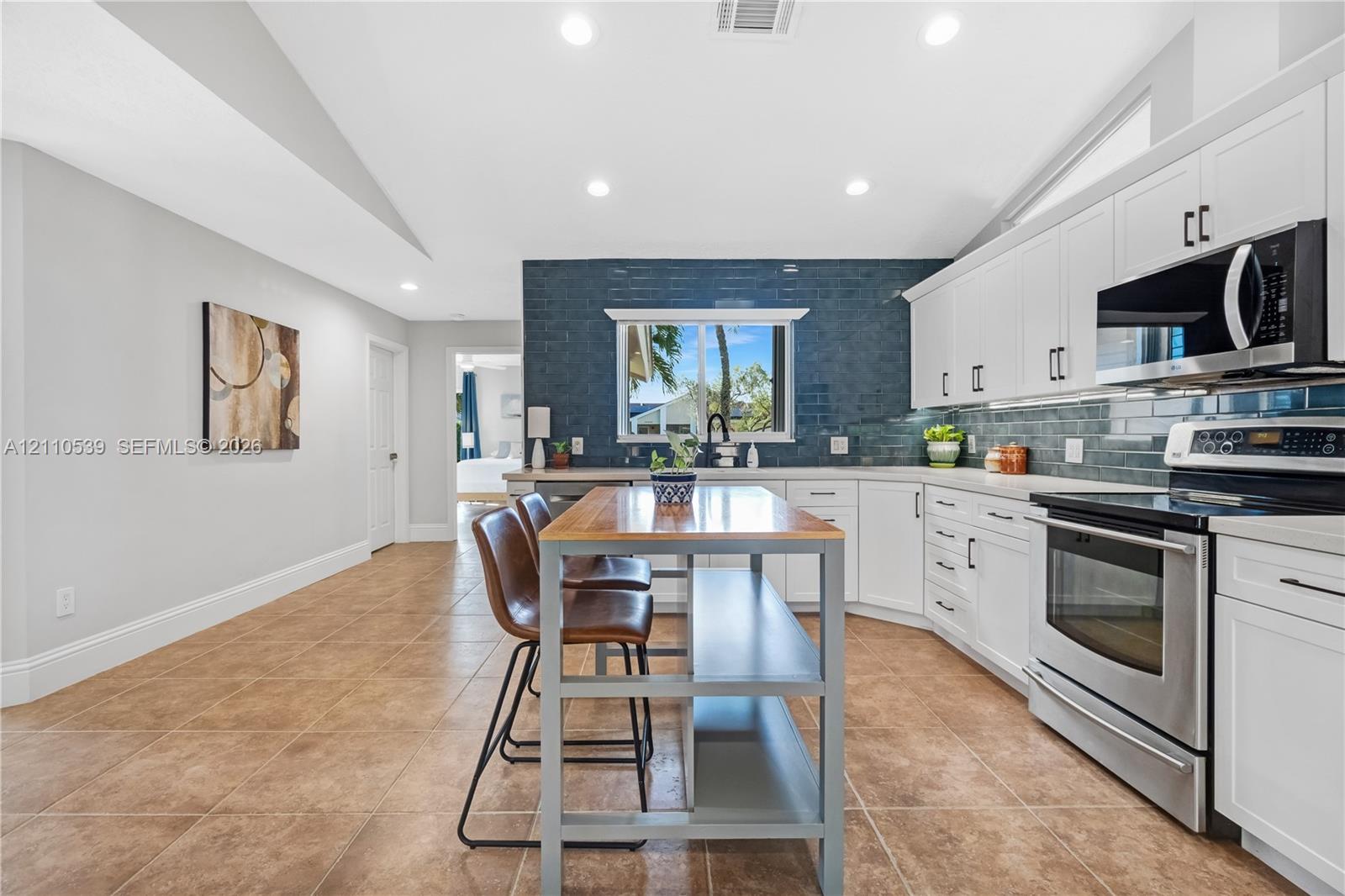 Kitchen featuring white cabinetry, blue tiled backsplash, stainless steel appliances, ceramic tile flooring, and vaulted ceilings with recessed lighting