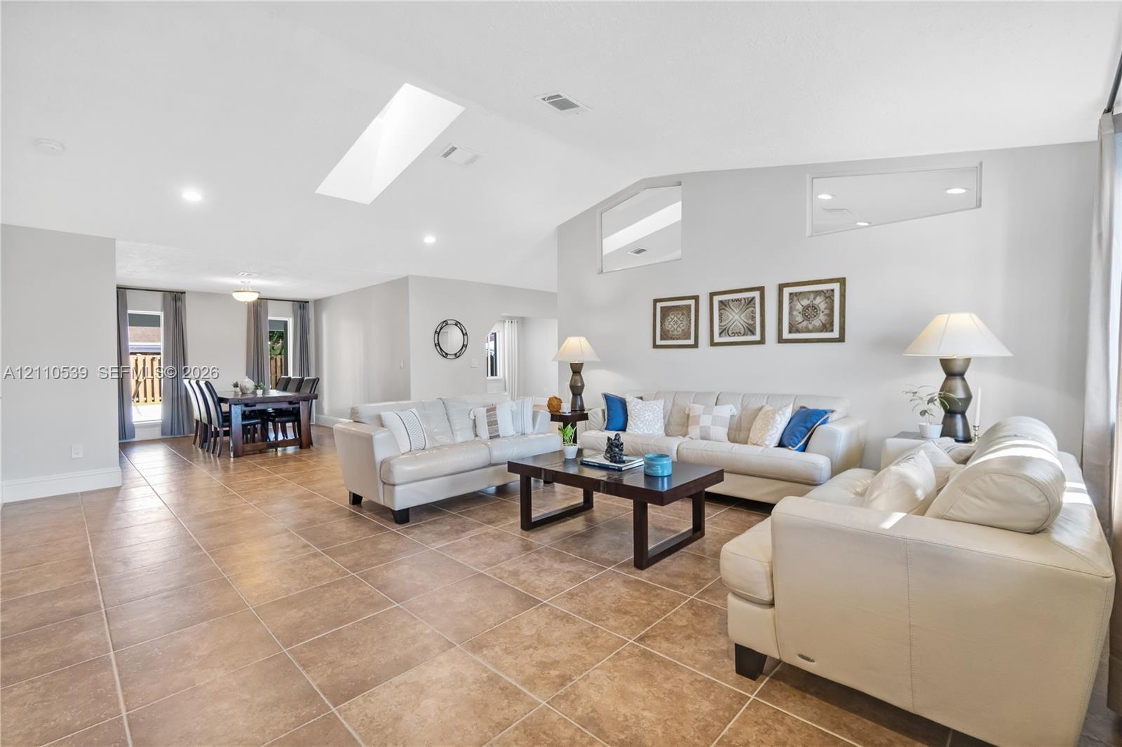 Open-concept living space featuring vaulted ceilings, a large skylight, high-set geometric windows, and tile flooring