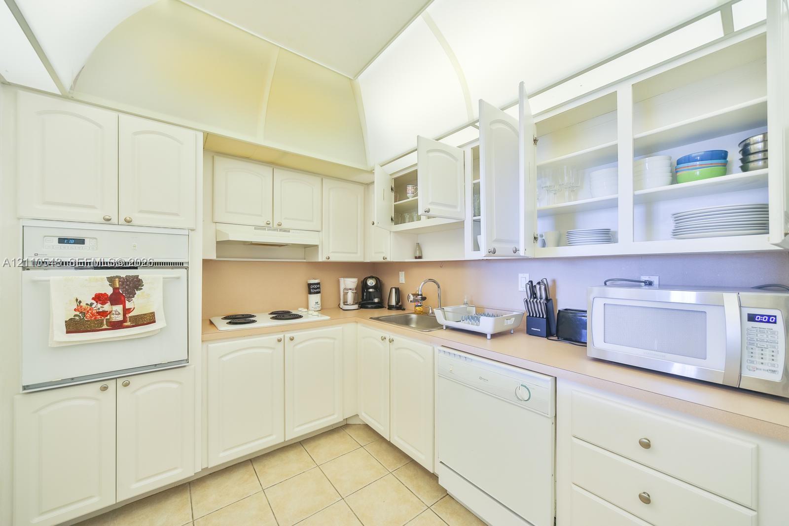 Kitchen featuring white cabinetry with glass-front display uppers, integrated wall oven, solid-surface countertops, and ceramic tile flooring