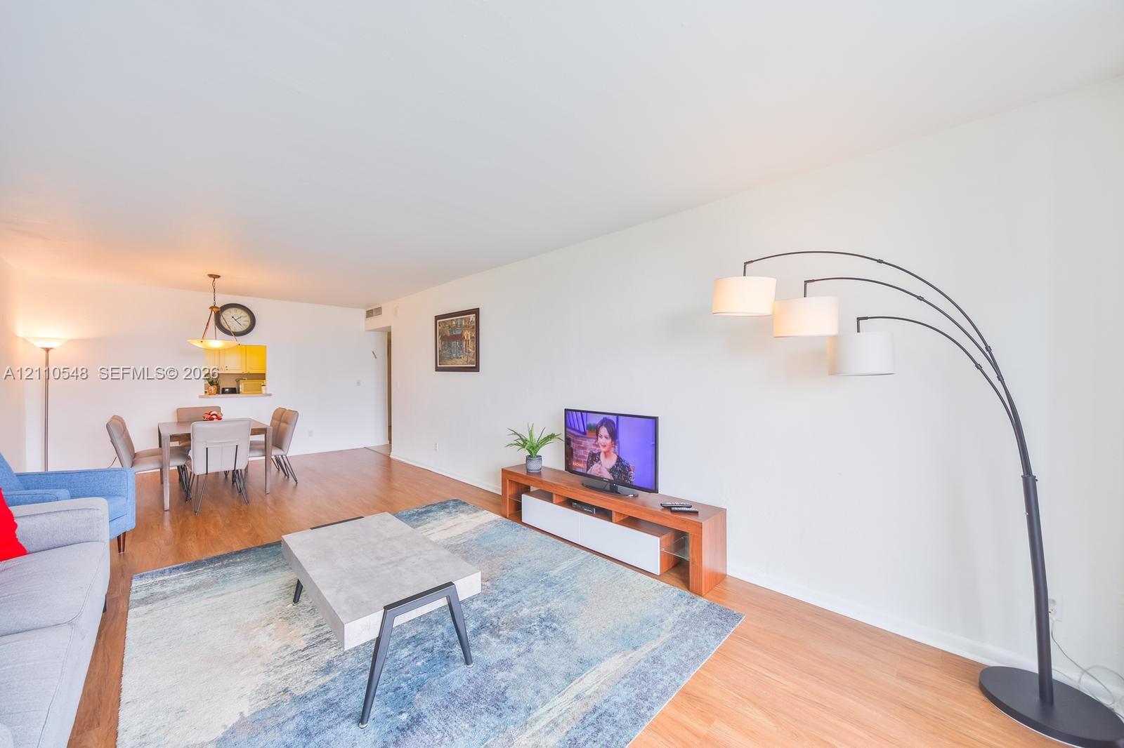 Open-concept interior featuring wood-finish flooring, smooth ceilings, and a kitchen pass-through window with a hanging pendant light fixture