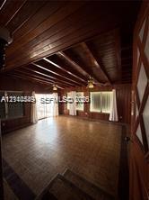 Interior space featuring natural wood-paneled walls, exposed wood-beam ceiling, grid-patterned tile flooring, and multiple windows