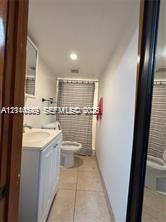 White vanity with a rectangular sink, neutral tile flooring, recessed ceiling lighting, and a bathtub with a shower enclosure