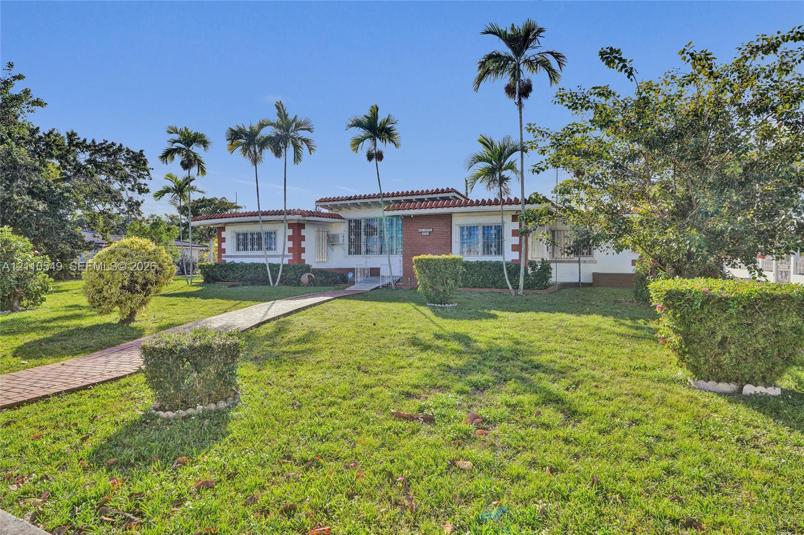 Single-story exterior featuring a brick facade with clay tile roof accents, accompanied by a paver walkway and established landscaping with mature palms
