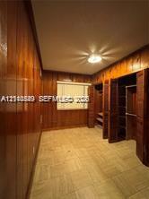 Room featuring vertical wood-paneled walls, tile flooring, recessed ceiling lighting, and built-in closet storage with louvered doors