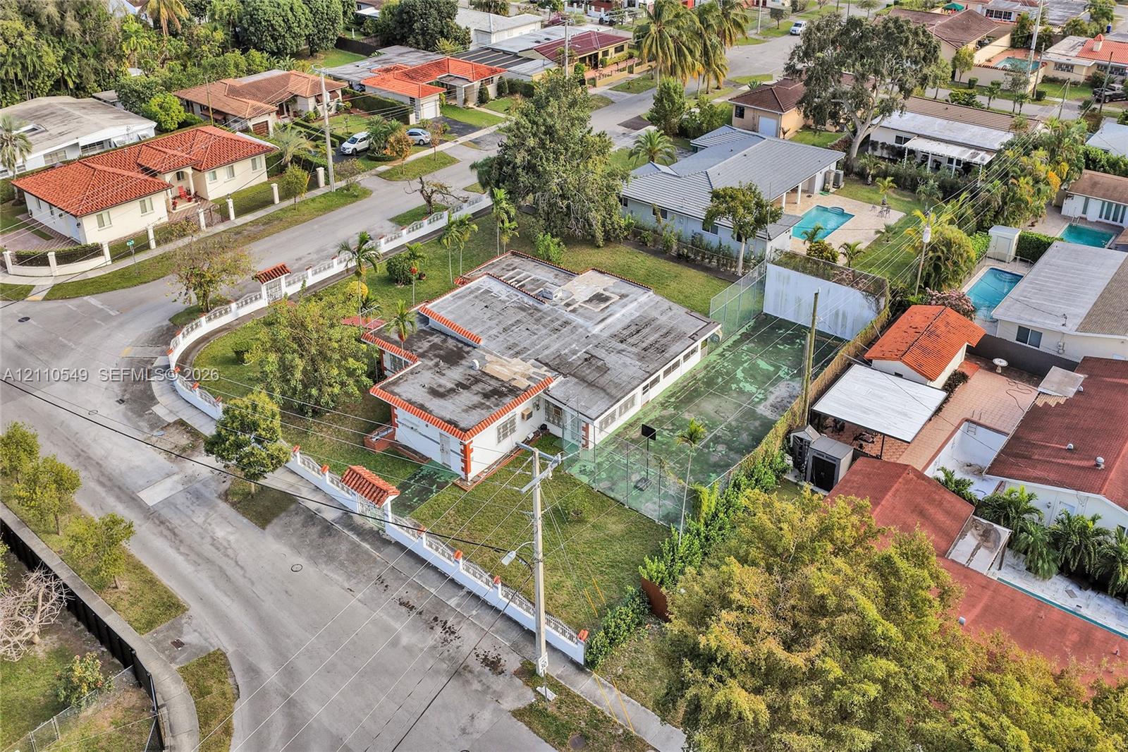 Aerial perspective featuring a corner lot property with a private fenced tennis court and a perimeter masonry wall
