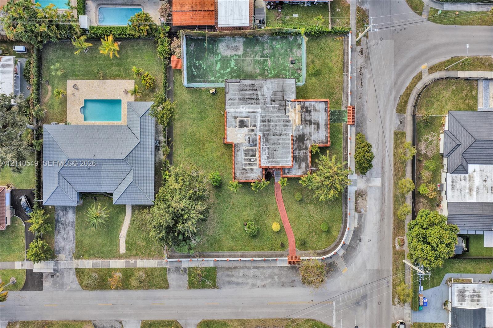 Aerial view of the property featuring a private fenced-in tennis court, expansive lawn, and paved walkway