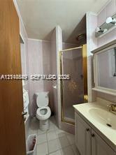 Bathroom featuring a vanity with integrated sink, brass-tone hardware, a wall-mounted medicine cabinet with integrated lighting, a stand-up shower enclosure with glass door, and tile flooring