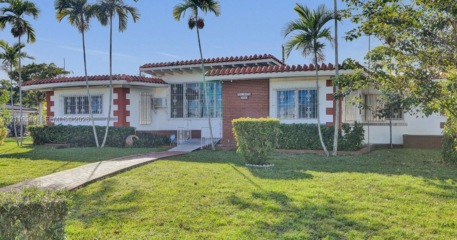 Single-story residence featuring a tile roof, brick masonry accents, white stucco exterior, and a paved walkway leading to the entryway Single-story residence featuring a tile roof, brick masonry accents, white stucco exterior, and a paved walkway leading to the entryway
