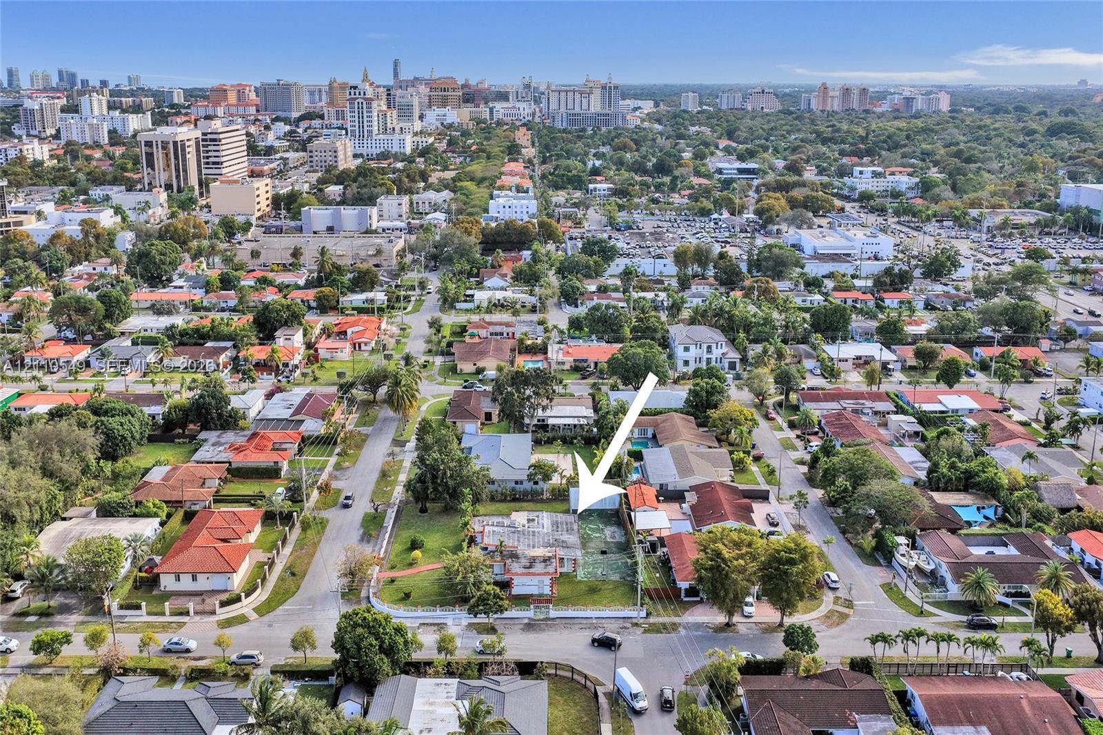 Aerial perspective of a corner lot featuring a residential structure, expansive lawn, mature landscaping, and a fenced perimeter